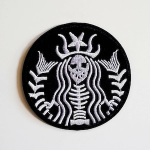 Könnte beinhalten: Ein gestickter Aufnäher in Schwarzweiß mit einer skelettartigen Meerjungfrau mit Krone, der dem Starbucks-Logo ähnelt.