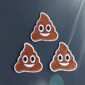 Może przedstawiać: Trzy brązowe haftowane łatki z emotikonami kupy z białymi obwódkami i uśmiechającymi się buźkami.