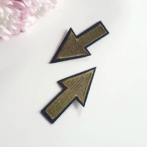 May include: Two gold embroidered arrow patches with black outlines. The arrows point in opposite directions.