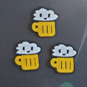 Puede incluir: Tres parches bordados para planchar que representan una jarra de cerveza amarilla con una nube blanca en la parte superior. La nube tiene una cara sonriente.