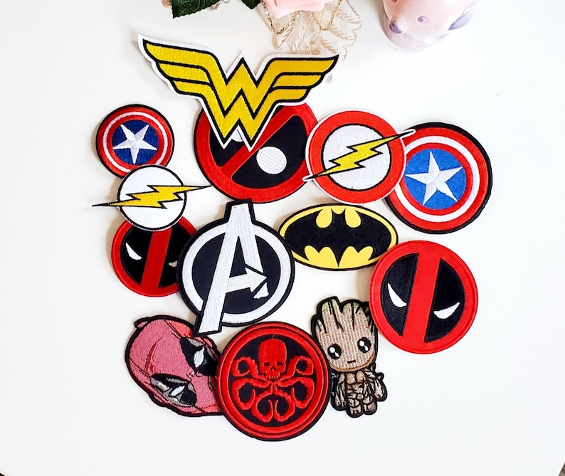 Puede incluir: Una colecci&oacute;n de parches bordados coloridos con logotipos y personajes de superh&eacute;roes. Incluye el logotipo de Wonder Woman, el escudo del Capit&aacute;n Am&eacute;rica, el emblema de Batman y la m&aacute;scara de Deadpool. Otros parches incluyen Flash, el logotipo de los Vengadores, Groot y una calavera roja.