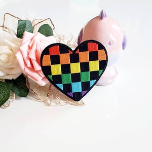May include: Rainbow checkered heart-shaped patch with a black background. The patch is made of fabric and has a stitched edge.