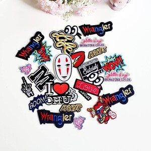 以下が含まれることがあります： 様々なデザインの刺繍入りアイロン接着パッチのセット。漫画のキャラクター、言葉、ロゴなどがあります。パッチには、「Wrangler」、「Paris」、「Subciety」、「Love」、「Boom」、「Mochi」、「Wow」、「Glitter is my Signature Color」、「Tattoo You」などの言葉が書かれています。