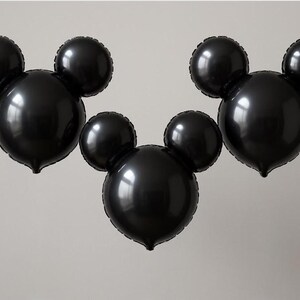 Puede incluir: Tres globos negros con forma de Mickey Mouse. Cada globo tiene una cabeza circular grande con dos orejas circulares m&aacute;s peque&ntilde;as en la parte superior. Los globos est&aacute;n inflados y parecen estar hechos de un material brillante, flotando sobre un fondo neutro.