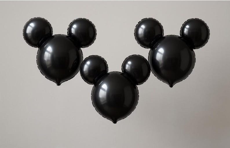 Puede incluir: Tres globos negros con forma de Mickey Mouse. Cada globo tiene una cabeza circular grande con dos orejas circulares m&aacute;s peque&ntilde;as en la parte superior. Los globos est&aacute;n inflados y parecen estar hechos de un material brillante, flotando sobre un fondo neutro.