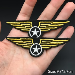 May include: Two black embroidered patches with yellow wings and a white star in a circle. The patches are 9.3 x 2.7 cm in size.