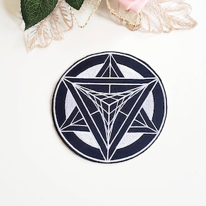 May include: A black and white embroidered patch featuring a geometric star design. The star is made up of overlapping triangles and is surrounded by a circle.