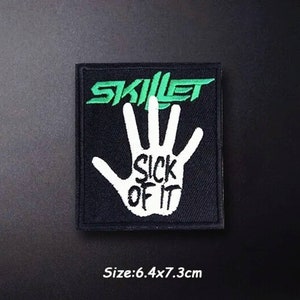 May include: Black embroidered patch with a white hand and the words "Sick of It" in green. The band name "Skillet" is written in green above the hand. The patch is 6.4 cm by 7.3 cm.
