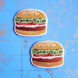May include: Two embroidered iron-on patches of a hamburger with lettuce, tomato, and sesame seed bun. The patches are on a blue background with a map.