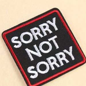 Puede incluir: Parche cuadrado negro con costuras rojas alrededor de los bordes. El texto "SORRY NOT SORRY" está bordado en blanco.