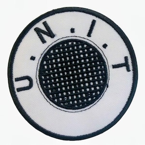 May include: Circular embroidered patch with a white background and a black border. The patch features the letters "N.I.T." and "U" in black, surrounding a black mesh circle. The design is simple and bold, suitable for various applications.