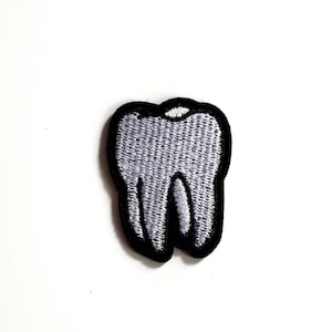 May include: Embroidered patch in the shape of a molar tooth. The tooth is light grey with a black outline. The patch is on a white background.