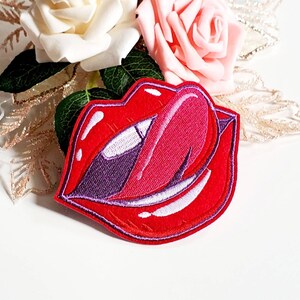 Könnte beinhalten: Roter gestickter Patch mit einem Paar Lippen, aus denen eine Zunge herausragt.