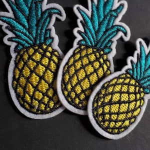 May include: Three embroidered pineapple patches with white felt backing. The pineapples are yellow with black outlines and have teal green leaves.