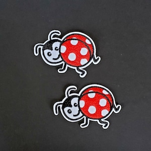 May include: Two red and white ladybug iron-on patches with black outlines and white spots. The ladybugs have black eyes and smiling faces.