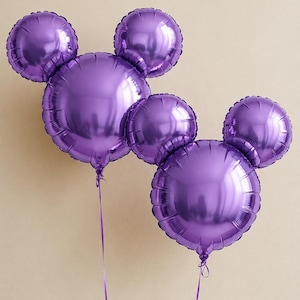 Peut inclure: Deux ballons en aluminium violet métallisé, chacun formé d'une grande tête circulaire avec deux petites oreilles rondes attachées au sommet. Chaque ballon possède un fin ruban violet noué à la base, formant une silhouette de tête de souris.