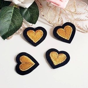 Può includere: Quattro toppe a forma di cuore in feltro nero con cuori ricamati in oro.