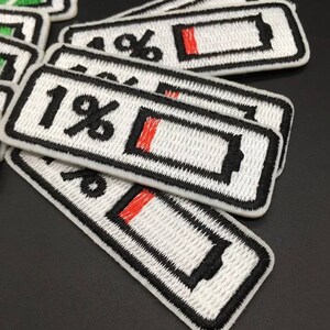 Puede incluir: Un conjunto de cinco parches termoadhesivos blancos con contornos negros y acentos rojos. Cada parche presenta un icono de batería con un símbolo de porcentaje, que va del 1% al 5%.