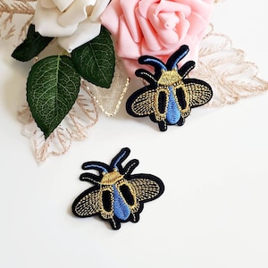以下が含まれることがあります： 青と金のミツバチの刺繍アイロン接着パッチ2枚。ミツバチは黒で金色のアクセントと青い羽根が付いています。