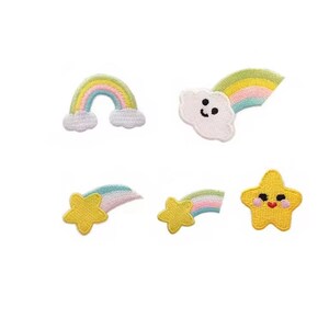 May include: A collection of five embroidered patches with playful designs. The set includes a rainbow, a cloud with a rainbow, and three yellow stars with rainbows. The patches are in pastel colours and have a stitched texture.