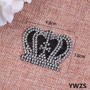Könnte beinhalten: Eine schwarze und silberne Strass-Kronenapplikation mit den Maßen 4,8 cm x 3,8 cm. Die Krone besteht aus kleinen Strasssteinen und hat eine spitze Spitze.
