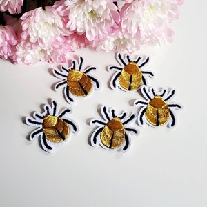 May include: Five gold embroidered iron-on patches of bugs with black outlines. The bugs are on a white background.
