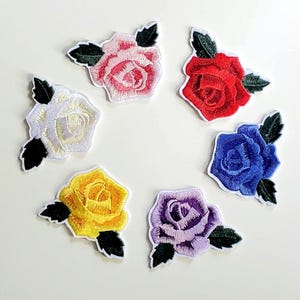 May include: Six embroidered iron-on patches featuring different colored roses. The roses are pink, red, white, yellow, blue, and purple.