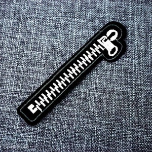 May include: Black zipper patch with white teeth. The zipper is closed and the pull tab is at the top.