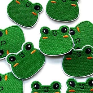 May include: A set of ten green felt frog patches with embroidered eyes and smiling mouths. The patches are approximately 5 cm in diameter.
