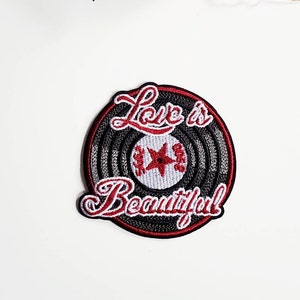 Op de afbeelding: Rode en witte geborduurde strijkpatch met een zwart-wit vinylplaatontwerp. De tekst "Love is Beautiful" is geborduurd in rood en wit.