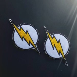 May include: Two white and yellow embroidered iron-on patches featuring the iconic lightning bolt symbol of the Flash superhero.