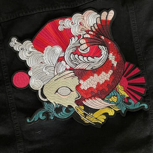 Puede incluir: Parche de hierro bordado con un pez koi rojo y blanco nadando a través de una ola con un sol rojo y blanco saliendo en el fondo.