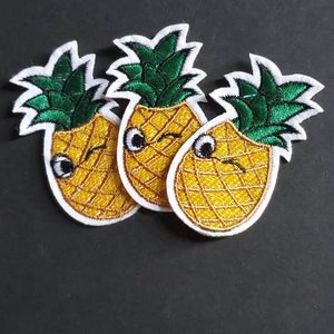 May include: Three embroidered pineapple patches with smiling faces. The pineapples are yellow with a grid pattern, green leafy tops, and white borders. The patches are on a black background.