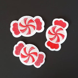 May include: Three red and white candy cane shaped patches with white stitching. The candy canes are in the shape of a traditional candy cane with a swirl design.