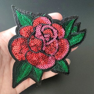 May include: A red and pink rose embroidered with sequins and green leaves. The rose is a popular motif for clothing and accessories.