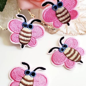 May include: Four pink and brown embroidered bee patches with black antennae and blue eyes.