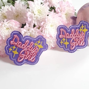May include: Two purple iron-on patches with the text "Daddy's Girl" in pink lettering and gold stars.