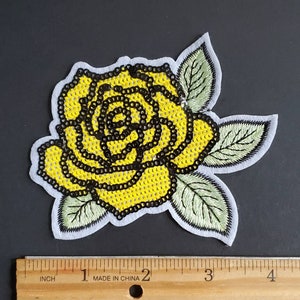 May include: A yellow sequined rose with green embroidered leaves. The rose is approximately 3 inches wide.
