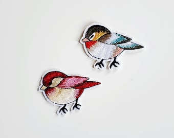 May include: Two embroidered iron-on patches of birds. One bird is red, white, and cream with a brown beak. The other bird is blue, green, white, and cream with a brown beak.