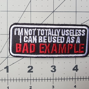 May include: Black embroidered patch with white and red stitching. The patch reads "I'm not totally useless I can be used as a bad example."