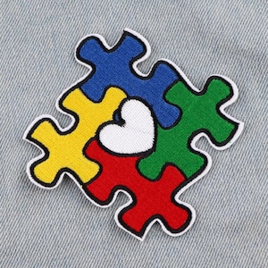 May include: A colourful jigsaw piece design with a white heart in the centre. The jigsaw pieces are blue, yellow, green, and red.