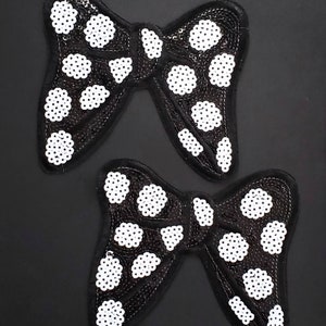 Peut inclure: Deux appliques en tissu noir en forme de nœud avec des pois blancs. Les nœuds sont faits de paillettes et sont parfaits pour ajouter une touche d'éclat à n'importe quel projet.