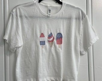 May include: White cropped t-shirt with red, white, and blue embroidered ice cream cones and popsicles.