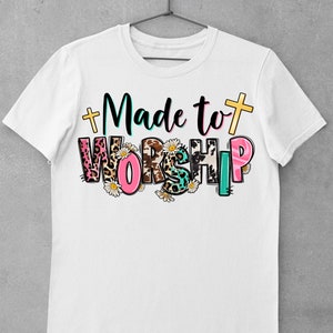 May include: White t-shirt with the text "Made to Worship" in colorful letters with animal print and floral accents.