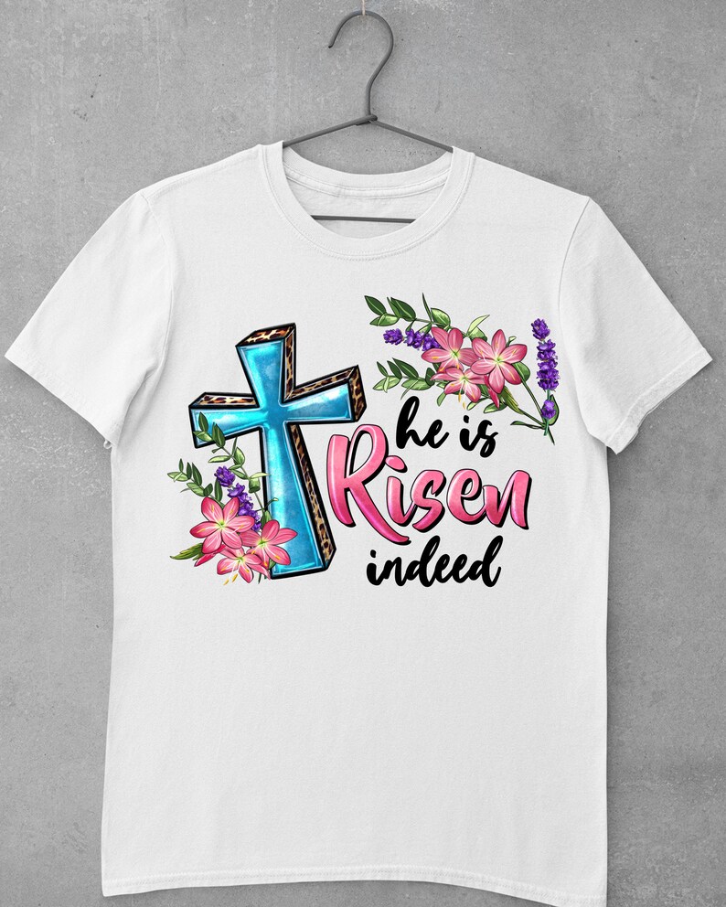 May include: White t-shirt with a blue cross with a leopard print design, pink flowers, and the text "He is Risen indeed".