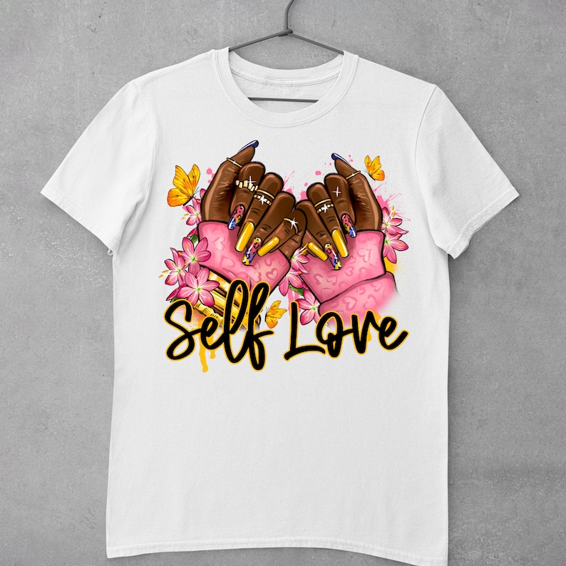 May include: White t-shirt with a graphic of two hands forming a heart shape with colorful nail polish and pink flowers. The text "Self Love" is written in yellow below the hands.