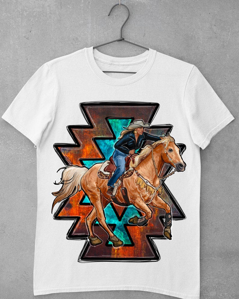 May include: White t-shirt featuring a graphic of a woman riding a horse. The horse is a light brown color, and the rider is wearing a cowboy hat and blue jeans. The graphic is set against a geometric design with orange, teal, and black accents.