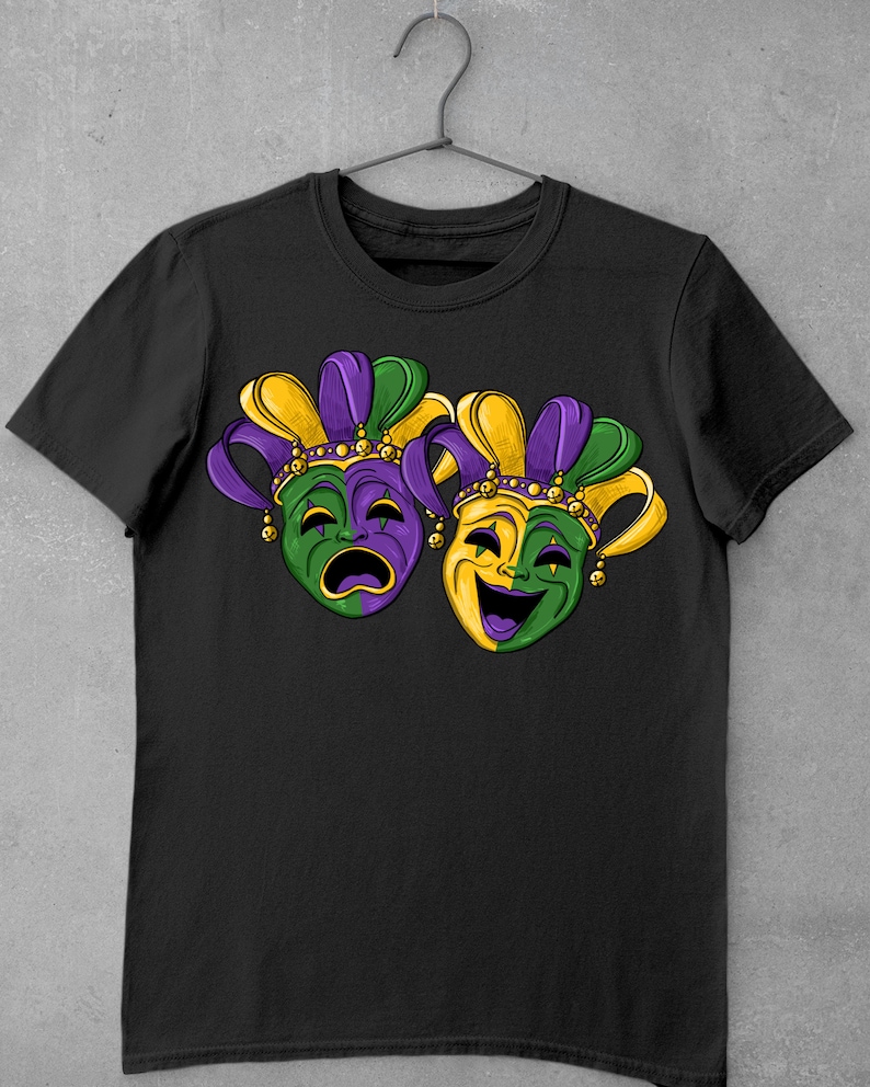 May include: Black t-shirt with a graphic of two Mardi Gras masks. One mask is green and purple with a sad expression, and the other is yellow and green with a happy expression.