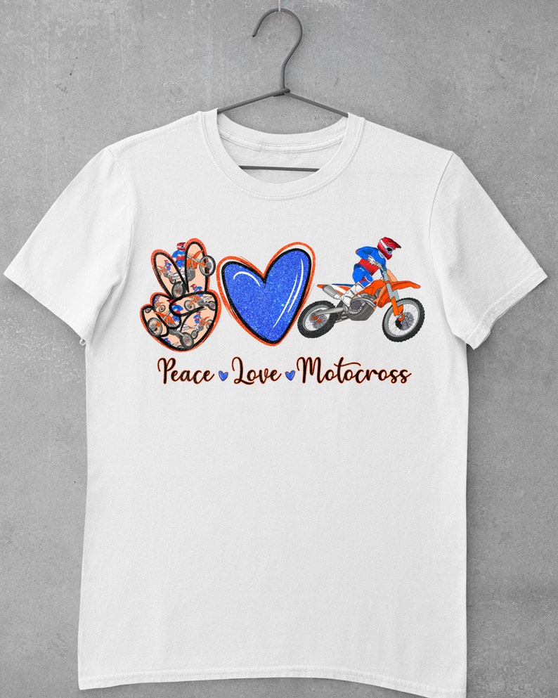 May include: White t-shirt with a peace sign, heart, and a motocross rider. The peace sign is made up of smaller motocross riders. The text "Peace Love Motocross" is below the design.