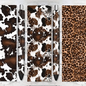 May include: Three different patterned pens with brown, black, and white designs. The pens are on a white wooden background.